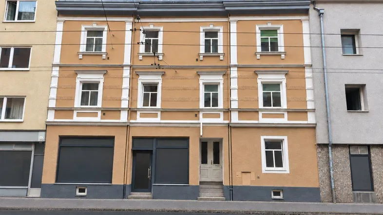 Klassisches Mehrfamilienhaus mit ockerfarbener Fassade und weißen Fensterrahmen an einer Straße.