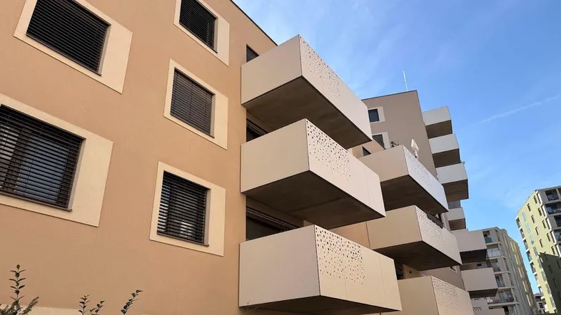Moderne Wohnhausfassade mit gestapelten Balkonen und Jalousien unter blauem Himmel.