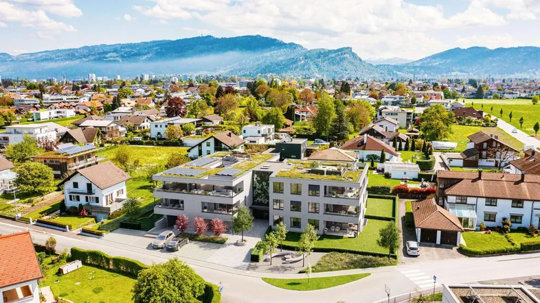 Luftaufnahme eines modernen Wohnkomplexes mit Gründächern in einer grünen Wohngegend mit Bergblick.