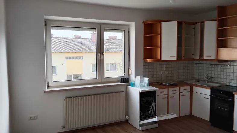 Küche mit Laminatboden, weißen und holzfarbenen Schränken, Spülmaschine und Fensterblick.