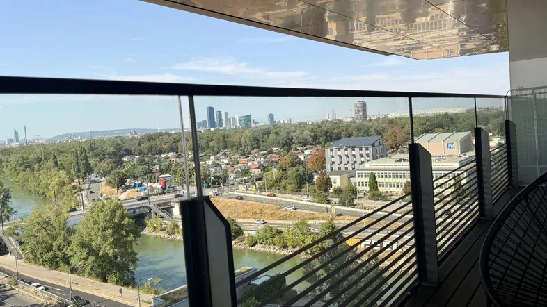 Geräumiger Balkon mit Glasbrüstung, Holzboden und weitem Blick über Fluss und Stadt.
