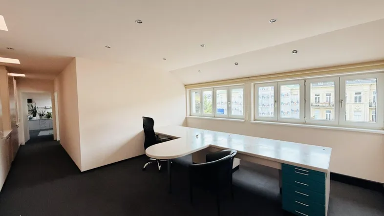 Geräumiges Büro mit Teppichboden, großen Fenstern und einem L-förmigen Schreibtisch.