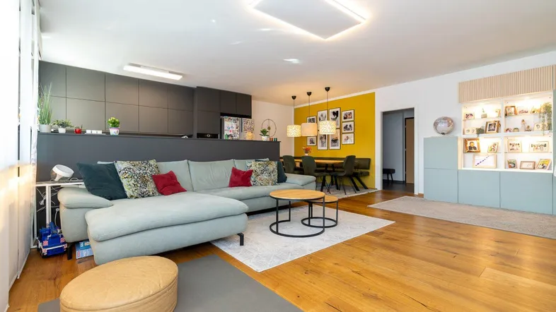 Geräumiger Wohn-Essbereich mit bequemer Couch, Holzboden und großen Fenstern.