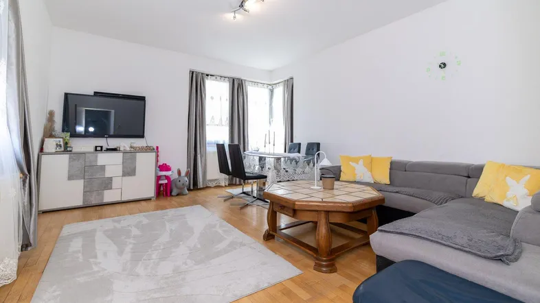 Helles Wohn- und Esszimmer mit Parkettboden, bequemer Couch und Esstisch am Fenster.