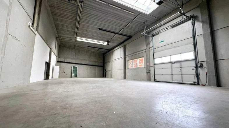 Geräumige Lagerhalle mit hohen Decken, Betonboden und großem Rolltor für Anlieferungen.