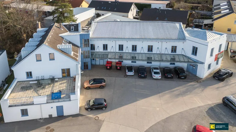 Luftaufnahme des Gebäudekomplexes mit großem Parkplatz und umliegenden Häusern.
