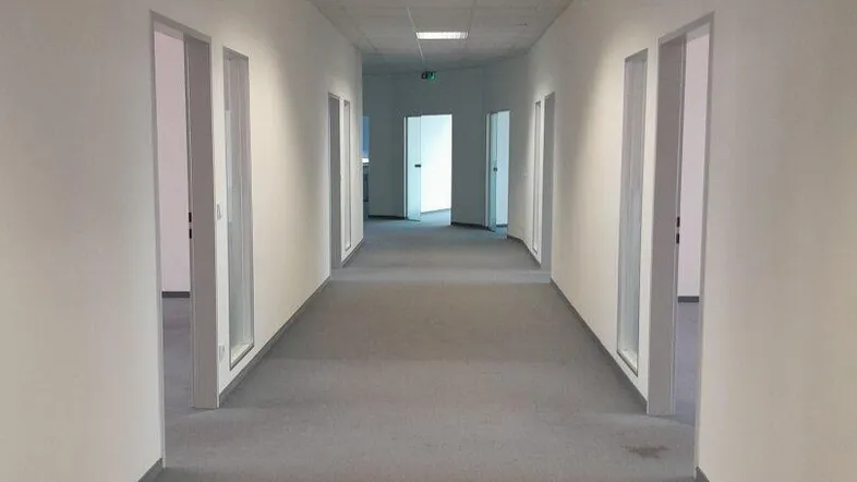 Langer, heller Flur mit grauem Teppichboden und mehreren Bürotüren auf beiden Seiten, gut beleuchtet.