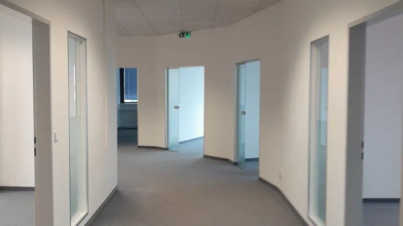Langer Bürogang mit Teppichboden und mehreren Türen zu den einzelnen Büroräumen, gut beleuchtet.