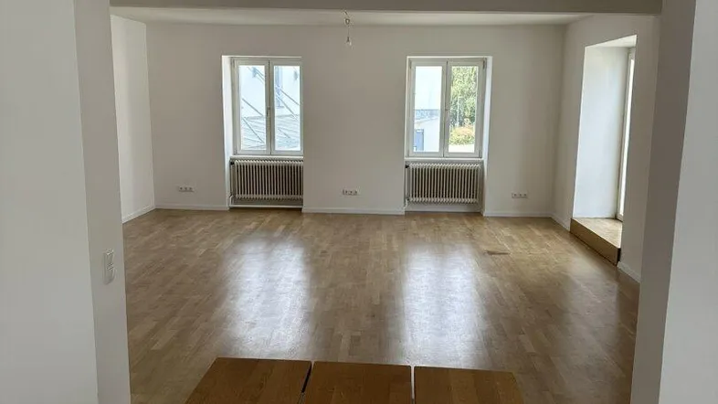Blick in einen weiteren hellen Raum mit zwei Fenstern und durchgehendem Parkettboden.