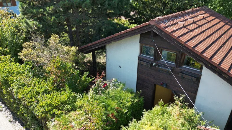 Luftaufnahme eines Hauses mit Ziegeldach, umgeben von dichtem Grün und hohen Bäumen.