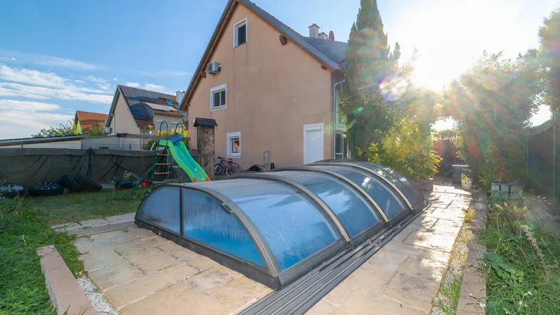 Hinterhof mit Poolüberdachung, Kinderrutsche und Rasenfläche unter strahlendem Sonnenschein.