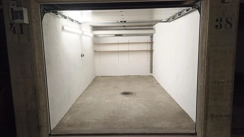 Leere Garagenbox mit Betonboden, weißen Wänden und praktischen Regalen für zusätzlichen Stauraum.