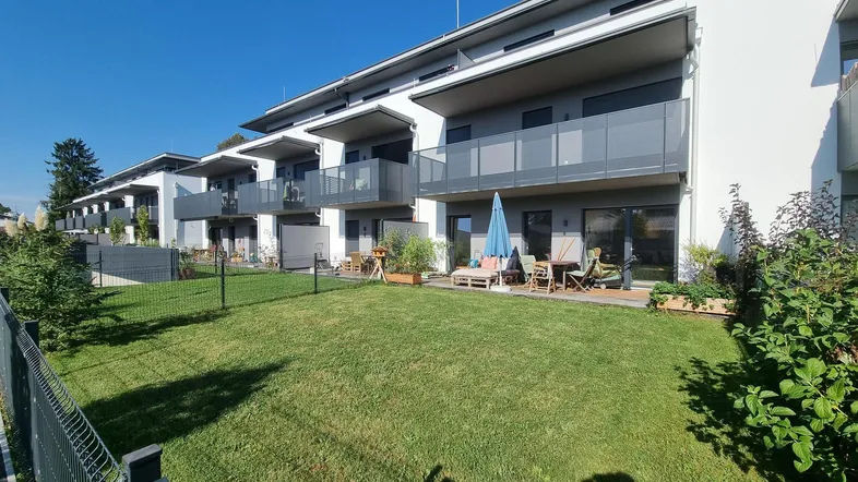 Moderne Wohnanlage mit mehreren Balkonen, Terrassen und gepflegten Grünflächen unter blauem Himmel.