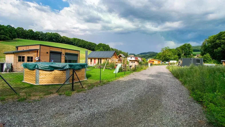 Blick auf eine ländliche Siedlung mit kleinen Häusern, Schotterweg und grünen Hügeln unter bewölktem Himmel.