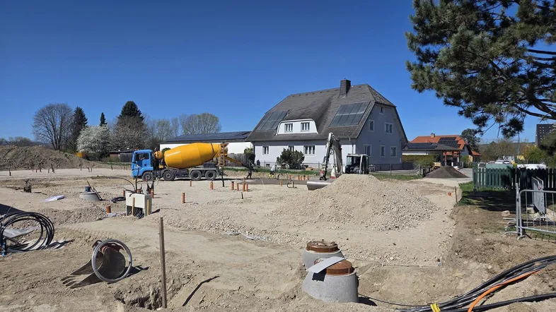 Baustelle für neue Wohnhäuser mit einem bestehenden Gebäude im Hintergrund unter blauem Himmel.