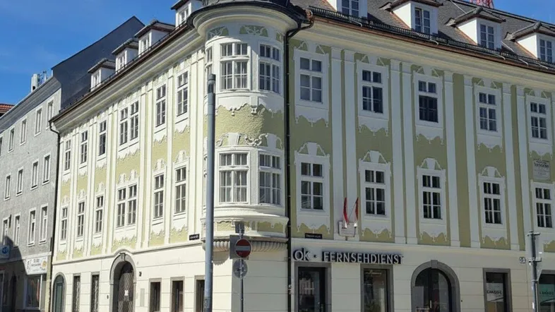 Historisches Gebäude mit markanter Eckfassade und Erker, in hellgrün und weiß gestrichen.