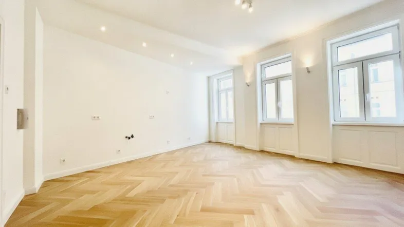Helles, leeres Zimmer mit Fischgrätparkett und mehreren Fenstern, bereit zur individuellen Gestaltung.