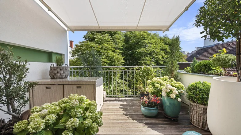 Geräumiger Balkon mit Holzboden, Markise und vielen Pflanzen, ideal zum Entspannen im Freien.