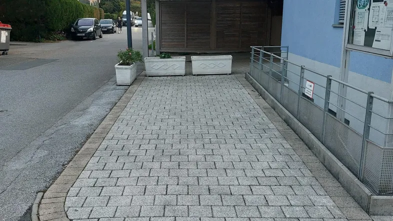 Gepflasterter Parkplatz vor einem modernen Gebäude mit Rampe und überdachtem Stellplatz.