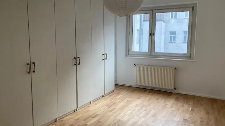 Helles Schlafzimmer mit Einbauschränken, Parkettboden und Blick auf die Stadt.
