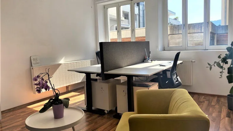 Helles Büro mit zwei Arbeitsplätzen, einem gelben Sessel und großen Fenstern, die viel Tageslicht hereinlassen.