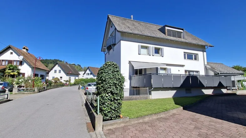 Weißes Einfamilienhaus mit Satteldach und Balkon in einer ruhigen Wohngegend.