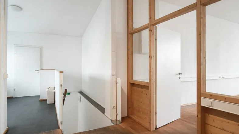 Heller Flur mit Holzboden, einer Treppe und einer Holztrennwand mit Glaselementen.