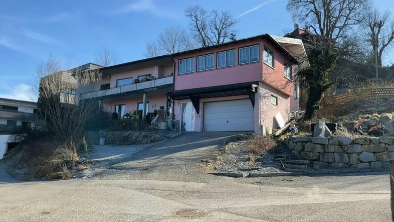 Rosa gestrichenes Haus mit Garage und Balkonen an einem sonnigen Hang.
