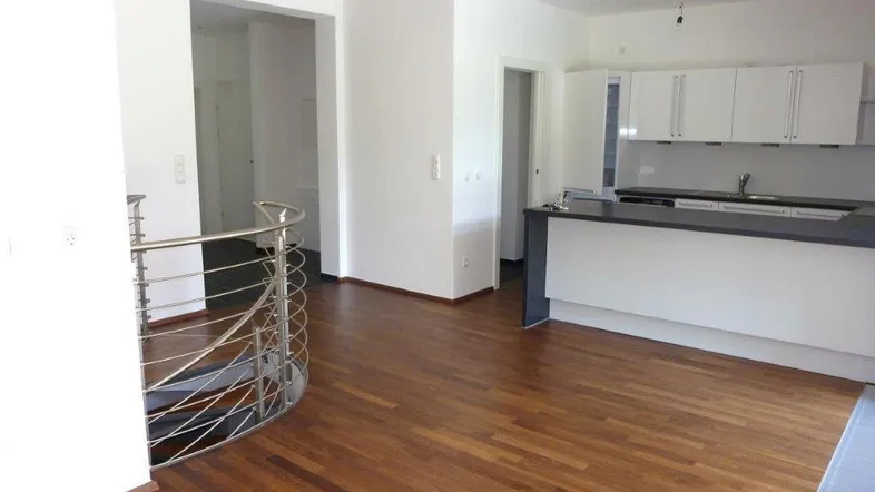 Heller offener Wohnbereich mit integrierter Küche, Holzfußboden und moderner Treppe.