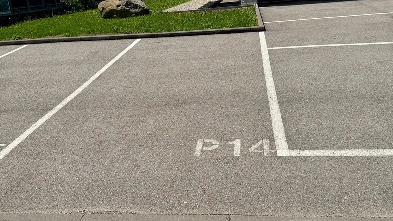 Außenparkplatz mit markierten Stellplätzen vor einem modernen Gebäude mit Holzfassade und Balkonen.
