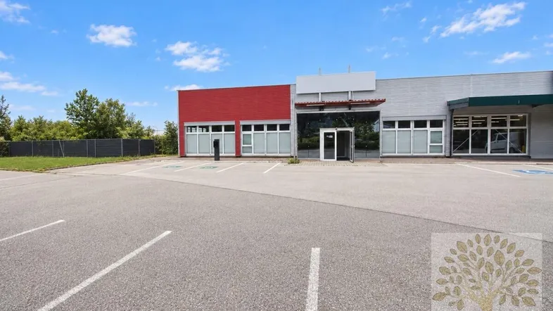 Modernes Geschäftsgebäude mit roter und grauer Fassade, großen Fenstern und einem weitläufigen Außenparkplatz.
