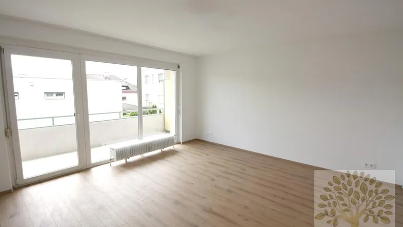 Helles Wohnzimmer mit Parkettboden und Zugang zu einem Balkon, ideal für entspannte Stunden.