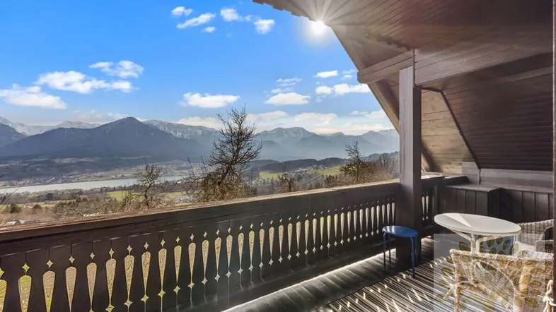Sonniger Balkon mit traditionellem Holzgeländer und atemberaubendem Blick auf Berge und See.