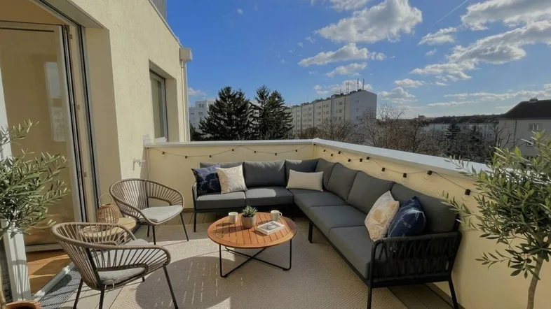 Geräumige Terrasse mit bequemen Loungemöbeln und Blick auf die Stadt unter blauem Himmel.