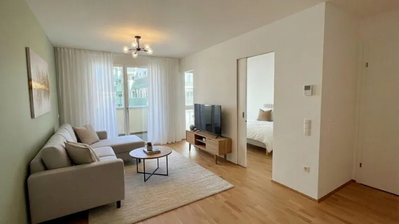 Helles Wohnzimmer mit modernem Sofa, Holzboden und Zugang zu einem Balkon.