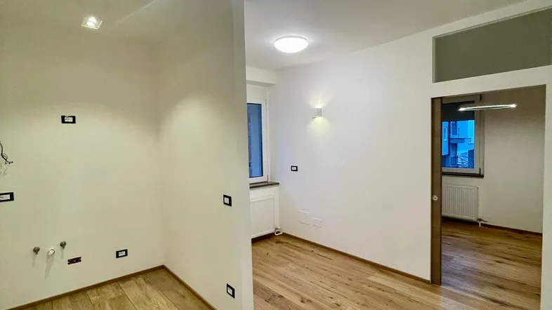 Heller, leerer Küchenbereich mit modernen Deckenleuchten und Holzoptik-Fliesenboden.