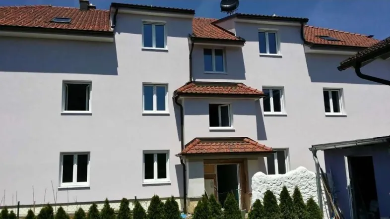 Mehrfamilienhaus mit heller Fassade, roten Ziegeldächern und vielen Fenstern in einer ruhigen Umgebung.