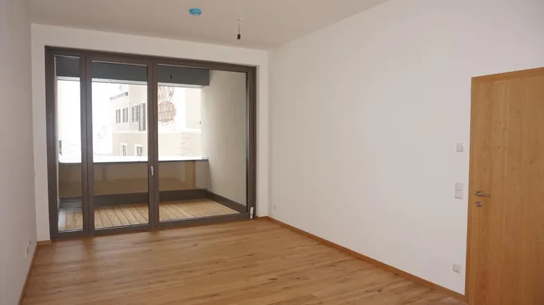 Helles Zimmer mit Holzboden und großen Glasschiebetüren, die zu einem kleinen Balkon führen.