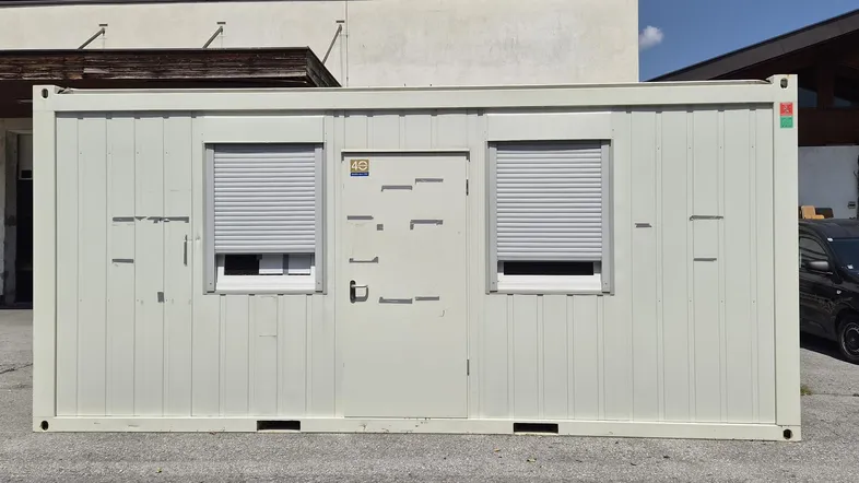 Vorderansicht eines weißen Bürocontainers mit Tür und zwei Fenstern, ausgestattet mit Rollläden.