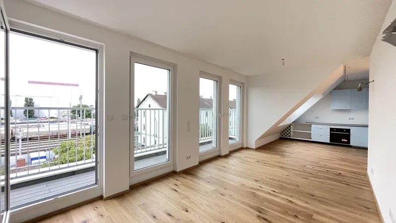 Helles Wohnzimmer mit Holzboden, Dachschrägen und Zugang zu einem Balkon mit Stadtblick.