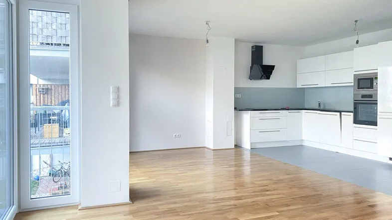 Heller offener Wohnbereich mit moderner Einbauküche und Parkettboden, ideal für modernes Wohnen.