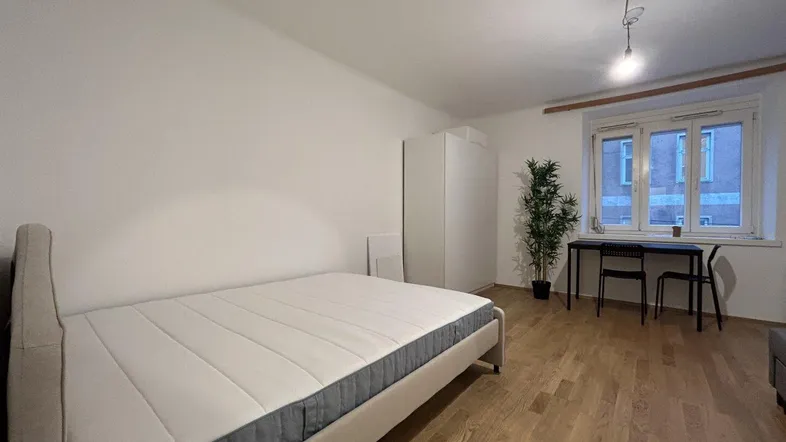 Helles Schlafzimmer mit Holzboden, großem Bett, Kleiderschrank und Schreibtisch am Fenster.