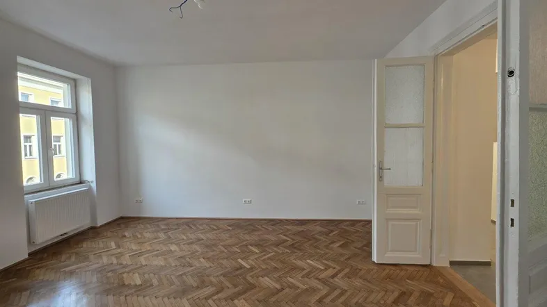 Helles Zimmer mit Fischgrätparkettboden und Blick auf die umliegenden Gebäude.