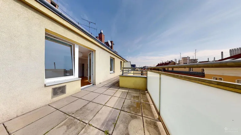 Große Terrasse mit Fliesenboden und Blick auf die umliegenden Gebäude unter blauem Himmel.