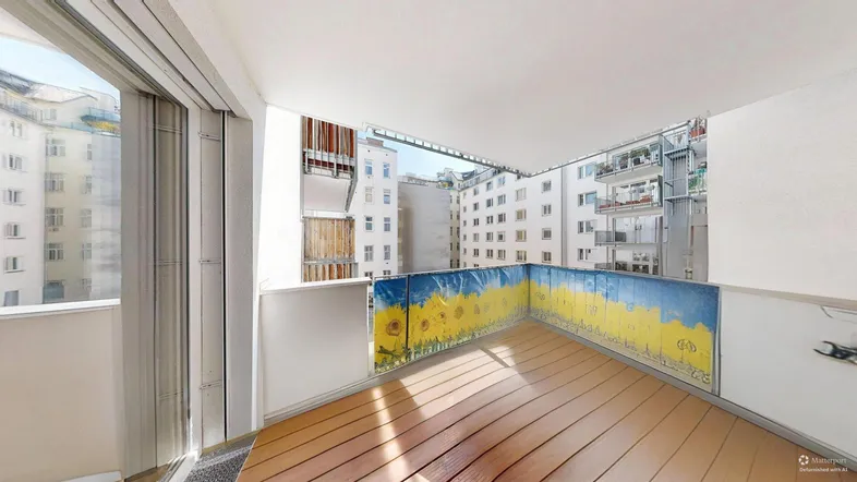 Heller Balkon mit Holzboden und Blick auf die umliegenden Gebäude, geschmückt mit Sonnenblumen.
