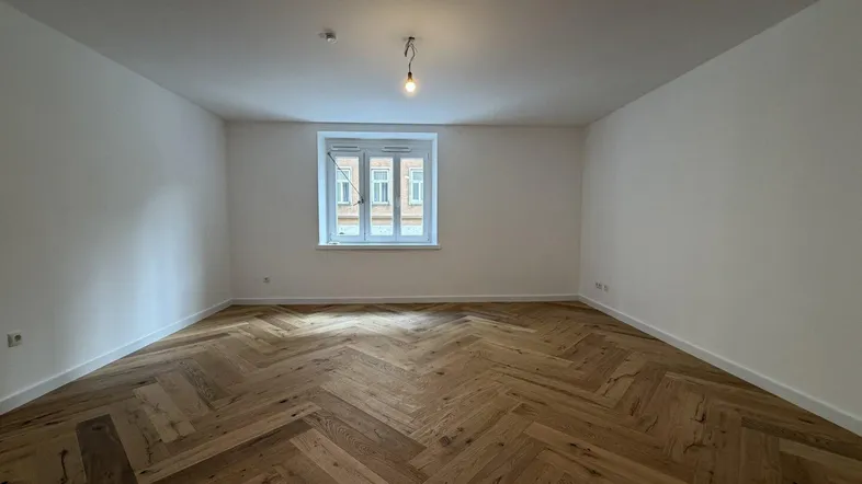 Helles Zimmer mit Fischgrätparkettboden und weiß gestrichenen Wänden, bereit zur Einrichtung.