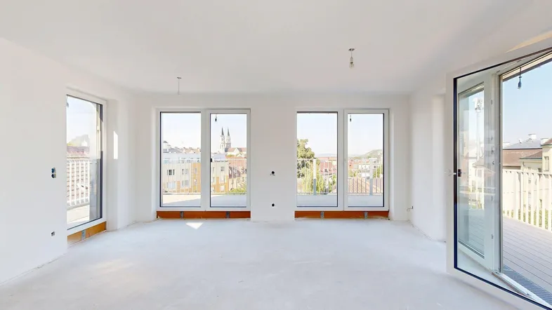 Helles, unfurniertes Zimmer mit großen Fenstern und Zugang zu einem Balkon, bietet einen weiten Stadtblick.