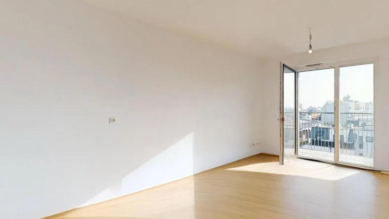 Helles, leeres Zimmer mit Holzboden und Zugang zu einem Balkon, ideal für Wohn- oder Schlafbereich.