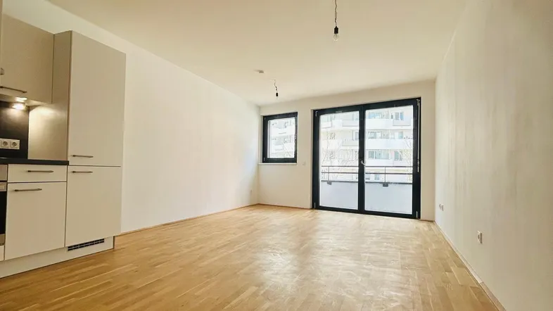 Heller Wohnbereich mit Eichenparkettboden, offener Küchenzeile und Zugang zum Balkon.