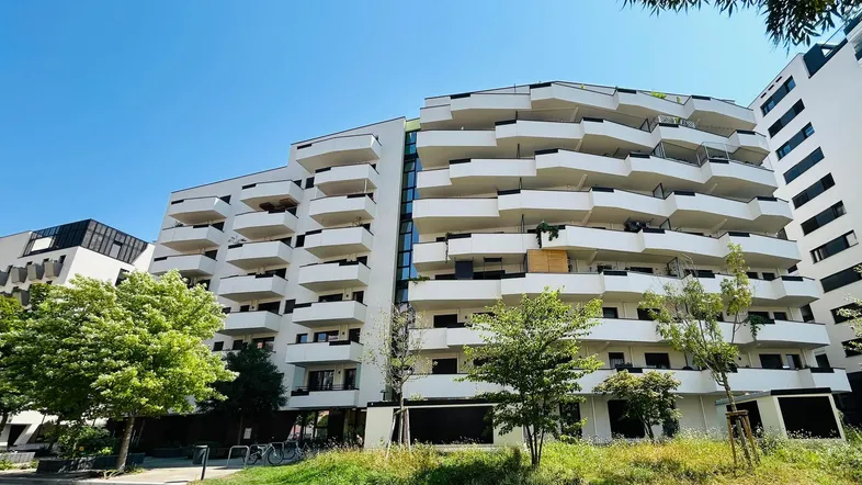 Moderne Wohnanlage mit vielen Balkonen und weißer Fassade unter blauem Himmel.